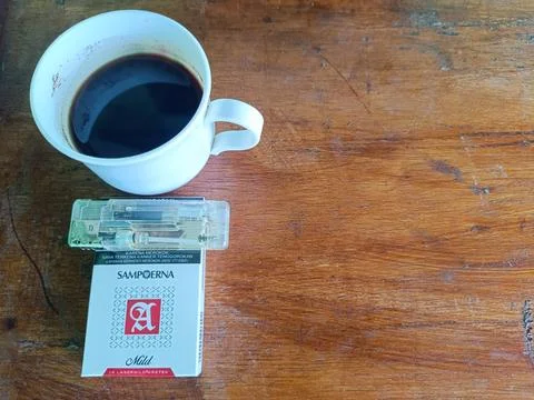 A cup of coffee, a pack of Sampoerna Mild cigarettes and a lighter on the table. Stock Photos