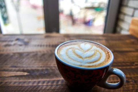 Cup of coffee with pattern on milk foam on a wooden table near the window Stockfoto's