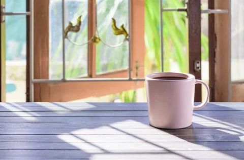 A cup of coffee is placed on the table by the window. and the morning sun in  Foto stock