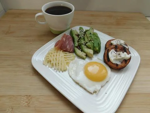 A cup of coffee, scrambled eggs, avocado, cheese, and ham on a white plate. h Stock Photos