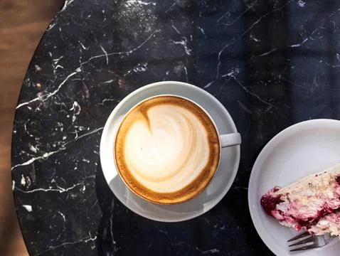 A cup of coffee sits on a table next to a slice of cake Stock Photos