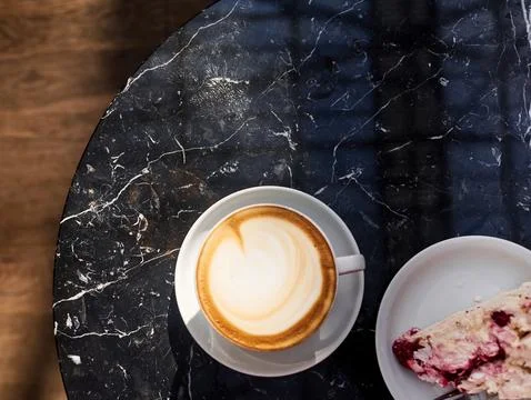 A cup of coffee sits on a table next to a slice of cake Stock Photos