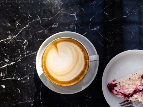 A cup of coffee sits on a table next to a slice of cake Stock Photos
