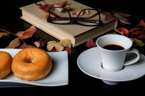 Cup of coffee with some glazed donuts, next to a book and reading glasses Stock Photos