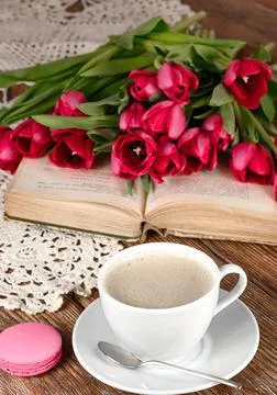 Cup of coffee, spoon, book, macaroon, tulips and knitted napkin on wooden table Stock Photos