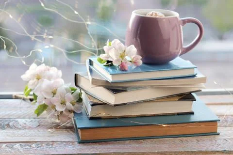 Cup of coffee, a stack of books, apple flowers on a wooden windowsill Stock Photos