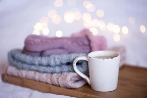 Cup of coffee with stack of knitted clothes over Christmas lights. Winter sea Stock Photos