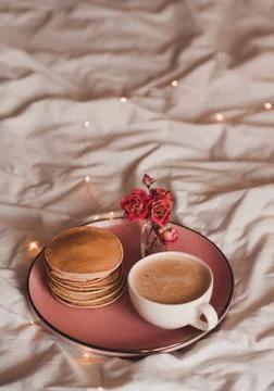 Cup of coffee with stack of pancakes on tray with dry flowers in bed. Good mo Stock Photos