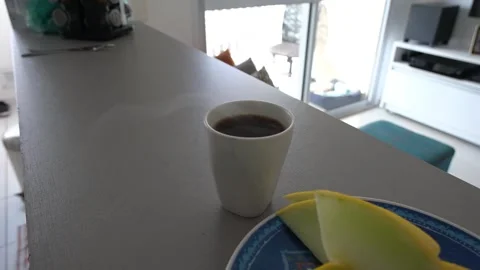 Cup of coffee steaming on the counter next to a plate with sliced ??melon. Stock Footage 312235728