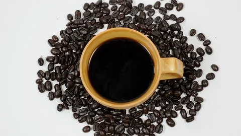 A cup of coffee surrounded by coffee beans on white background. Stock Footage 100792882