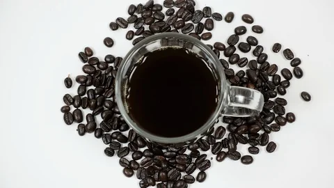 A cup of coffee surrounded by coffee beans on white background. Stock Footage 100795703