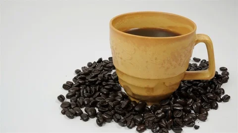 A cup of coffee surrounded by coffee beans on white background. Stock Footage 100796934