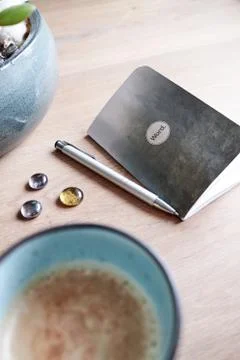 A cup of coffee on a table and note with a pen Stock Photos