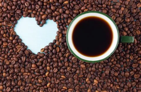 Cup of coffee on the table next to the heart painted in coffee beans Stock Photos