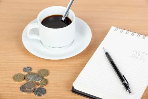 Cup of coffee on table with notepad and coinage Foto stock