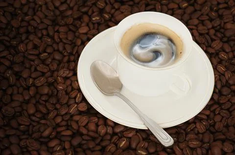 Cup of coffee with teaspoon on coffee beans background Stock Photos