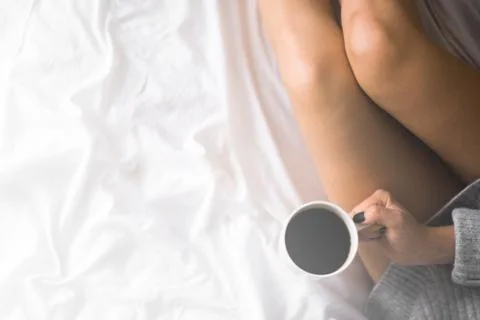 A cup of coffee in their hands in bed on a white blanket, simple, home, space 스톡 사진