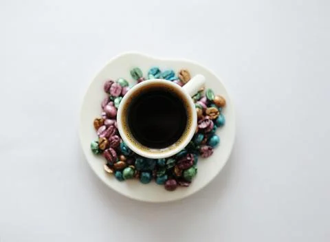 Cup of coffee top view. Multi-colored pearl coffee beans scattered around. White Stock Photos