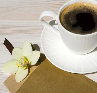 A cup of coffee on a white table. Envelope with Orchid. Romantic morning. Stock Photos