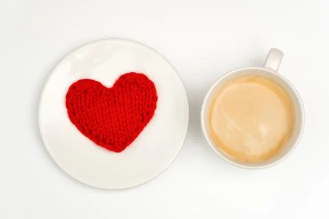 A cup of coffee is on a white table. There is a knitted red heart on the plat Stock Photos