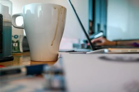 A cup of coffee on work desk with work stationary and laptop in the background Stock Photos