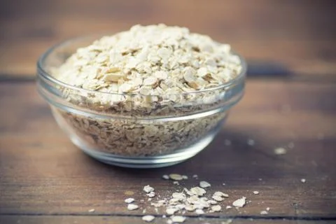 Cup of dry rolled oat flakes oatmeal on old wooden table Stock Photos