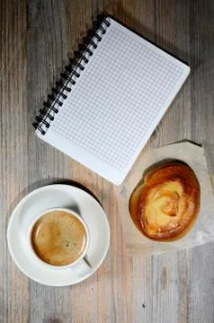 Cup of espresso, checkered notebook and bun Stock Photos