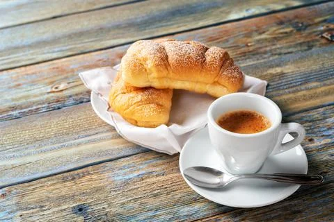 Cup of espresso coffee and brioche on an old wooden table. Stock Photos