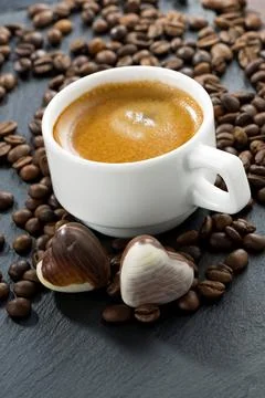Cup of espresso, coffee beans background and chocolate candies in a heart s.. Stock Photos