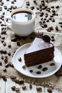 Cup of espresso, coffee beans on table with sackcloth, piece of chocolate cake Stock Photos