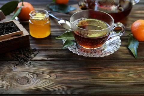 Cup filled with aromatic tea beside honey, citrus fruits, and dried tea leaves Stock Photos