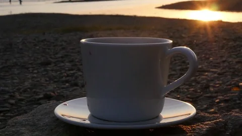 A cup of fragrant coffee stands on a rock by the river with a view of the golden Stock Footage 81179752