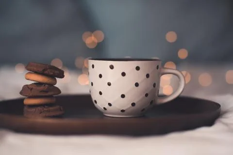 Cup of fresh hot tea with stack of chocolate cookies on wooden tray in bed cl Stock-Fotos