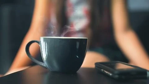 Cup of fresh hot tea on table with woman in blur background Stock Photos