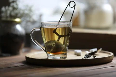 Cup of freshly brewed tea with snap infuser and sugar cubes on wooden table.. Stock Photos