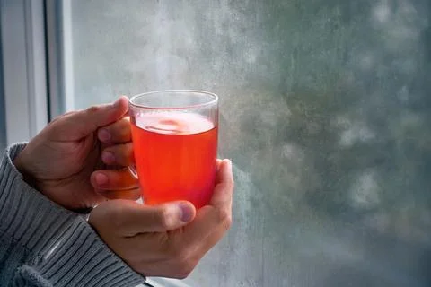 Cup of fruit tea in female hands near the window. Stock Photos