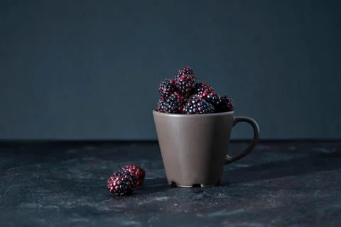 Cup full of blackberries on a dark surface. Dark food photography. Stock Photos