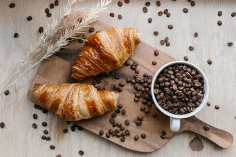 Cup full of coffee beans and two croissants on wooden board Stock Photos