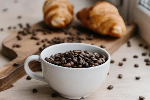 Cup full of coffee beans and two croissants in the background Stock Photos