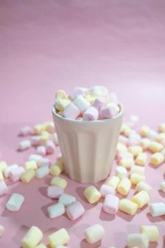 Cup full of tiny colored marshmallows and a lot of marshmallows around it on Stock Photos