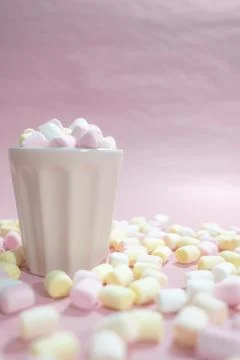 Cup full of tiny colored marshmallows and a lot of marshmallows on the table Stock Photos