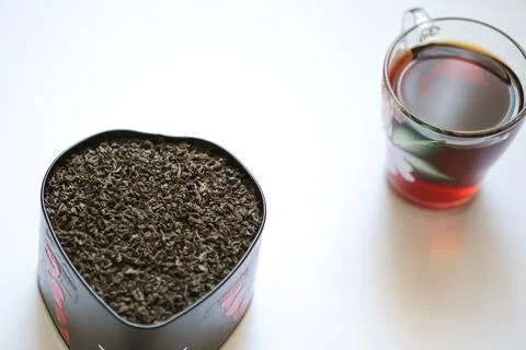 A cup of hot black tea with a container of tea leaves on a white background Stock Photos