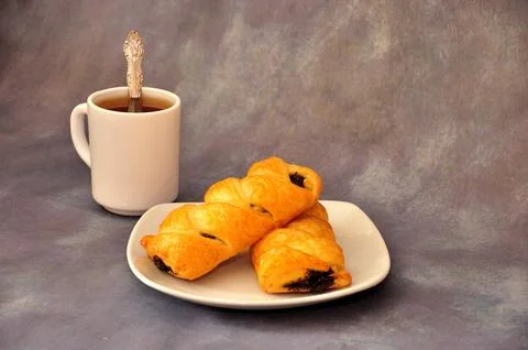 A cup of hot black tea with a spoon and a plate with two fresh spiral poppy.. Stock Photos