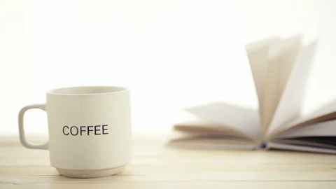 A cup of hot coffee with blurred open book as background 库存影片 107770725