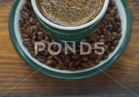 A cup of hot coffee with foam on a saucer with coffee beans Stock Photos
