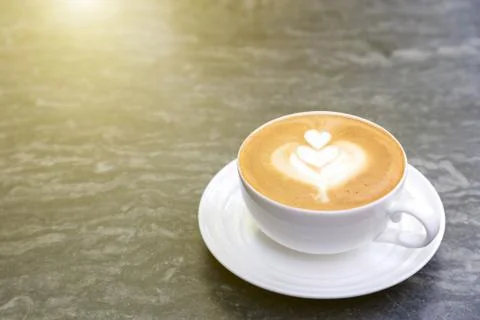 Cup of hot coffee with heart pattern in white cup on stone table background. Stock Photos