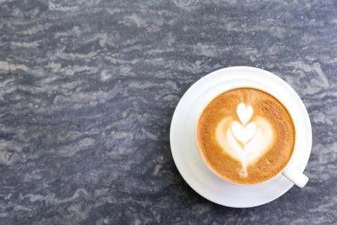 Cup of hot coffee with heart pattern in white cup on stone table background. Stock Photos