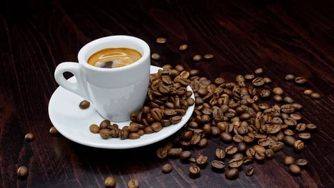 A cup of hot coffee with roasted beans around on a black background in 4k Stock Footage 91090046