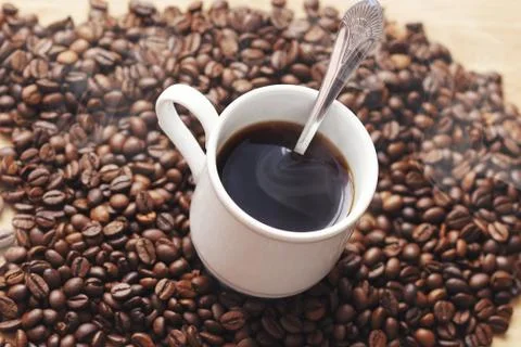 A Cup of hot coffee with the spoon inside on the background of coffee beans a Stock Photos