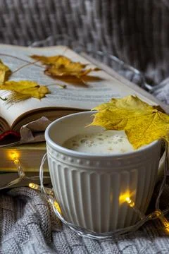 A cup of hot coffee a stack of books and yellow maple leaves on a knitted pla Stock Photos